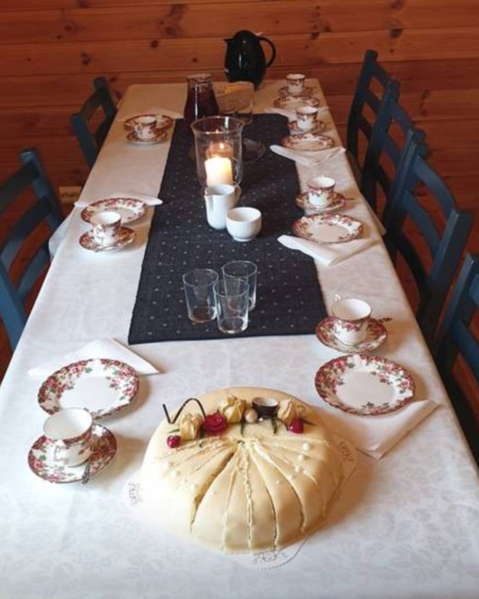 Fint pynta bord pynta med kvit duk, kaffiservice, lys og ei marsipankake